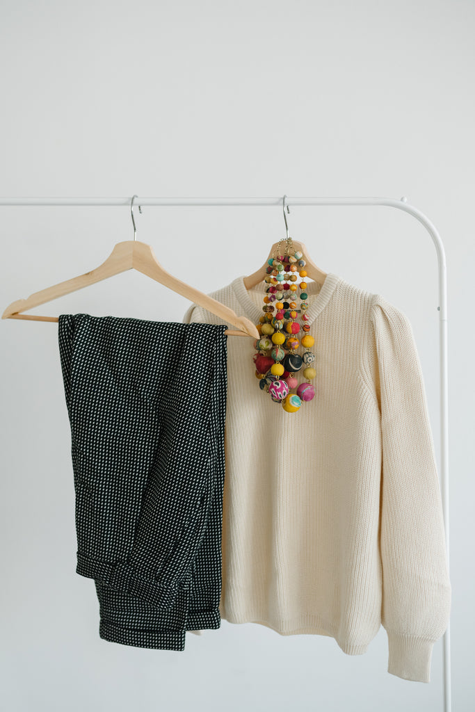 Sustainable checkered pants and a cream knit sweater paired with handmade jewelry hanging on wooden hangers. - Terra Shepherd - Sustainable and ethically made women's clothing including tops, dresses, pants, shoes, accessories, intimates, and more.